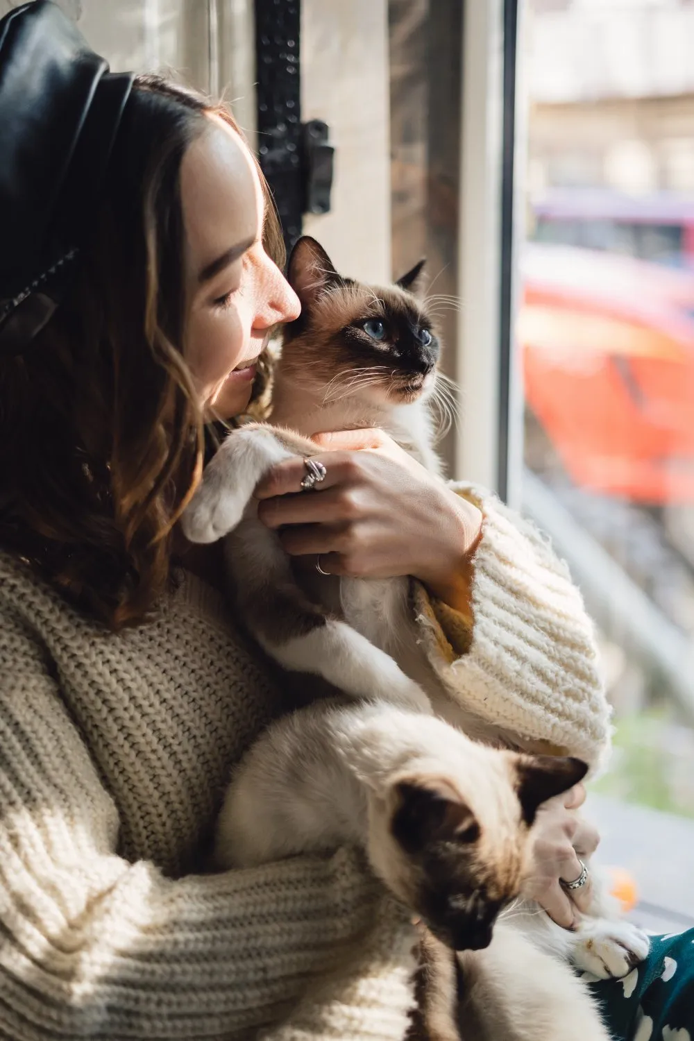 A woman cuddling a Siamese cat at home